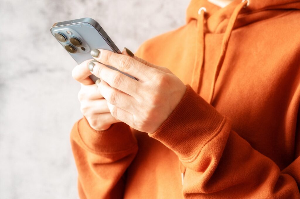 Woman in orange hoodie watches video on her smartphone.