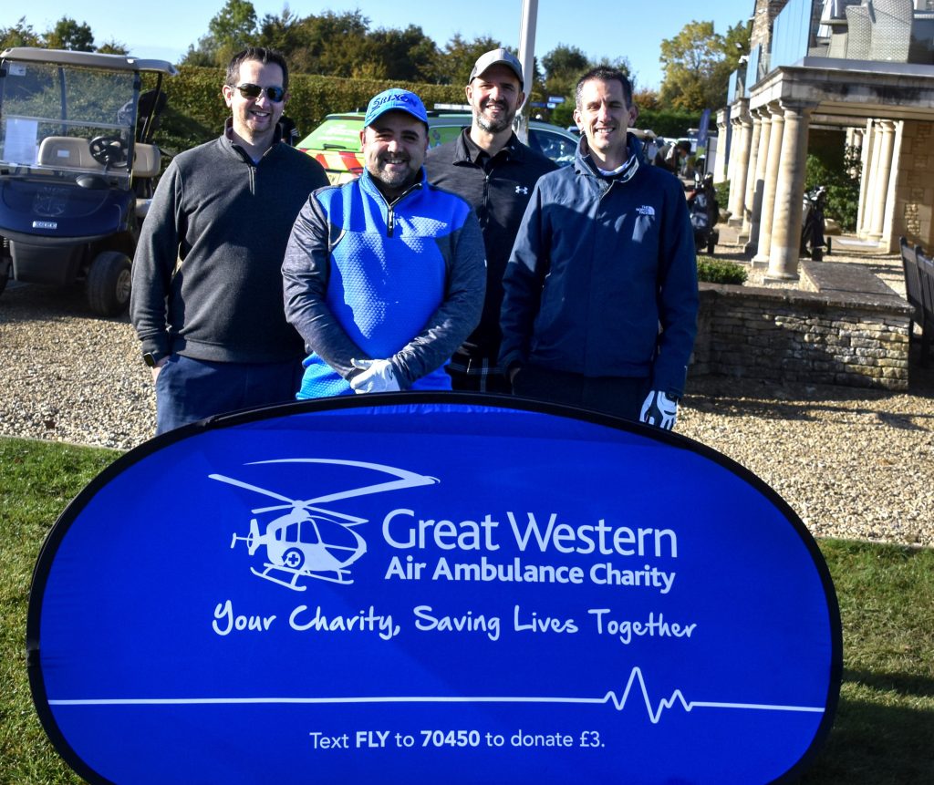 Four men stand with an air ambulance promotional banner