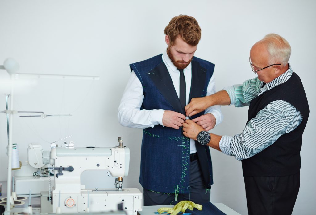 A tailor fits a man with a jacket