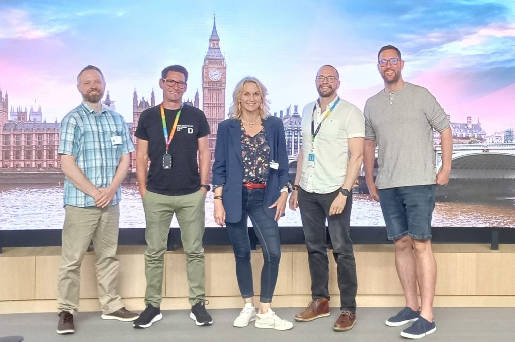 Five people stand relaxed in front of a London backdrop