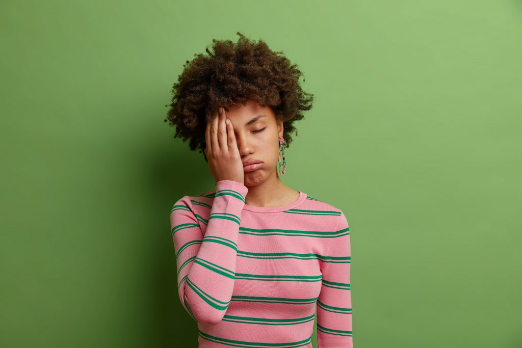 A woman looks tired in front of a green background 